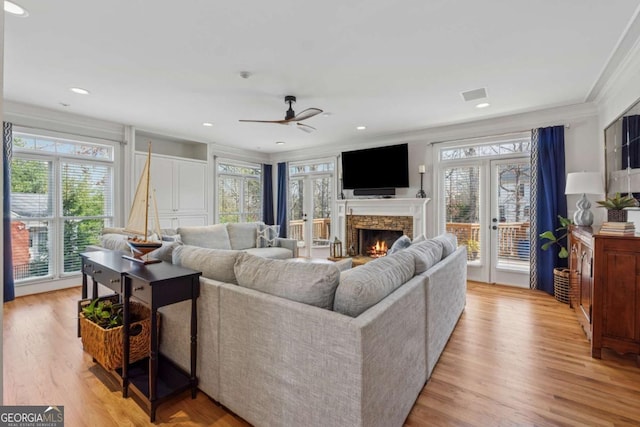 living area with a stone fireplace, visible vents, ornamental molding, french doors, and light wood finished floors