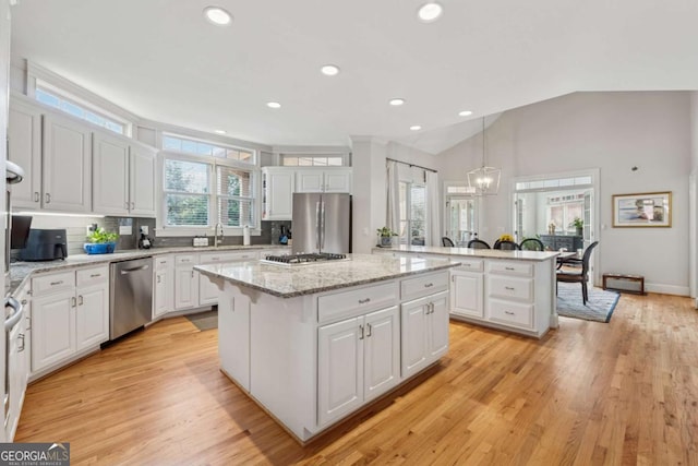 kitchen with stainless steel appliances, lofted ceiling, white cabinetry, and a kitchen island