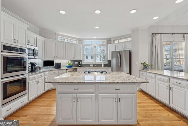 kitchen with a healthy amount of sunlight, appliances with stainless steel finishes, white cabinets, and a center island