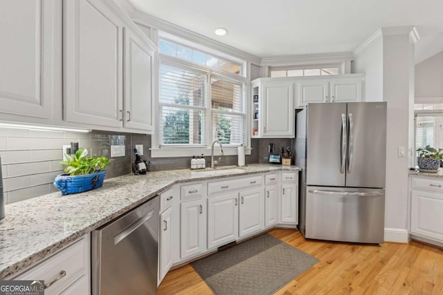 kitchen with tasteful backsplash, white cabinets, light wood-style flooring, stainless steel appliances, and a sink