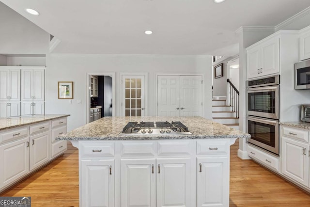 kitchen with light wood-type flooring, a kitchen island, white cabinets, and stainless steel appliances