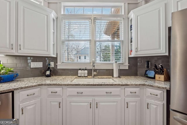 kitchen featuring white cabinetry, backsplash, a sink, and freestanding refrigerator