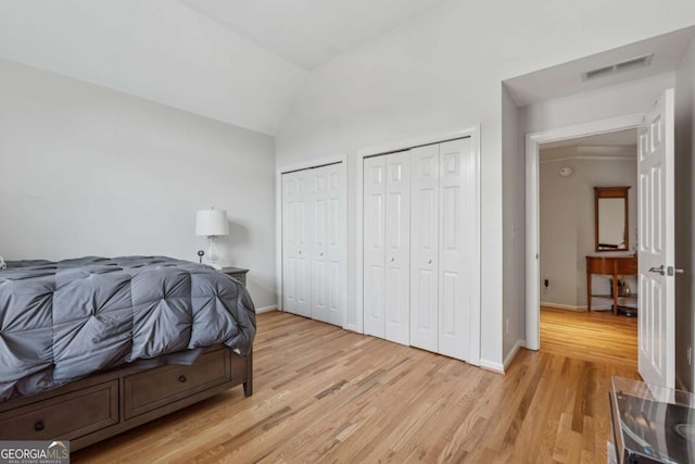 bedroom with baseboards, visible vents, vaulted ceiling, light wood-type flooring, and two closets