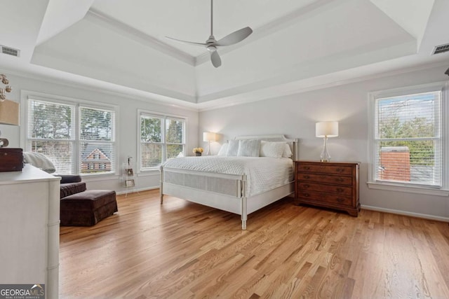 bedroom featuring a tray ceiling, visible vents, light wood-style flooring, and baseboards