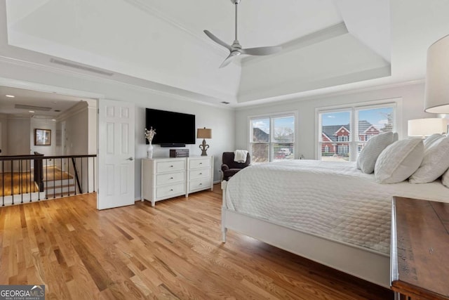 bedroom with ornamental molding, a tray ceiling, and light wood-style flooring