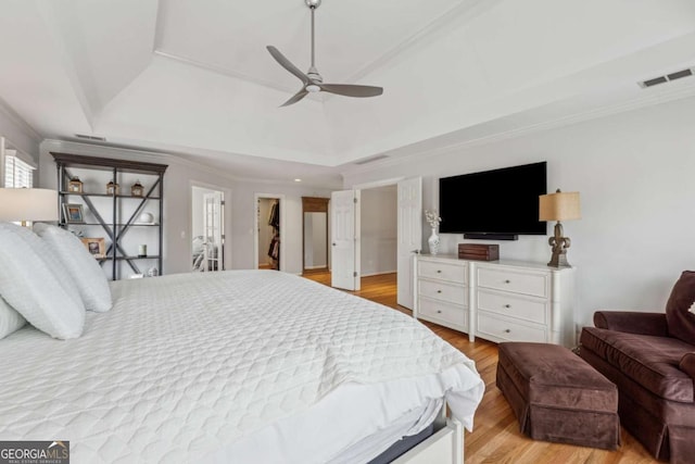 bedroom with a tray ceiling, visible vents, crown molding, and light wood finished floors