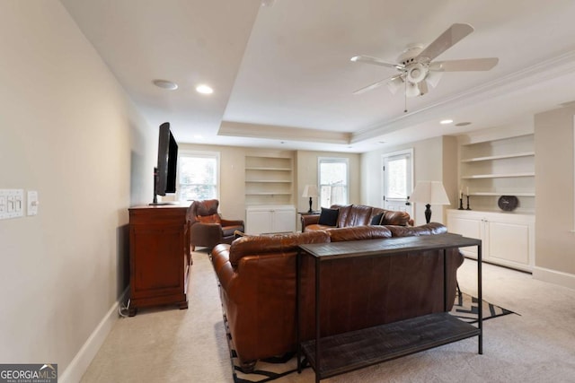 living area featuring built in features, a tray ceiling, a ceiling fan, light carpet, and baseboards