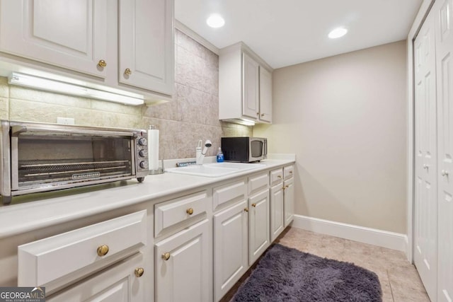 kitchen with tile patterned flooring, white cabinets, stainless steel microwave, and backsplash