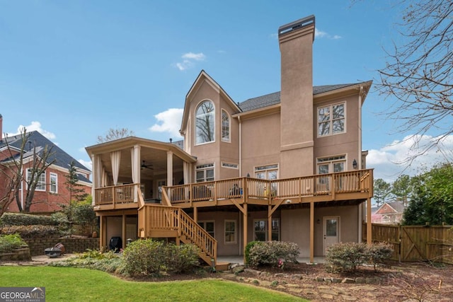 rear view of house with fence, stairs, a wooden deck, stucco siding, and a chimney