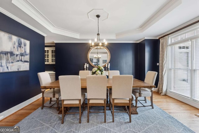 dining space with a chandelier, a raised ceiling, crown molding, and wood finished floors