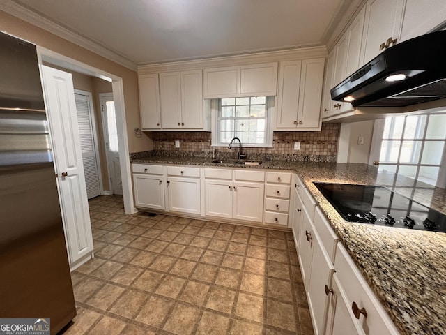kitchen featuring under cabinet range hood, black electric stovetop, backsplash, a sink, and freestanding refrigerator