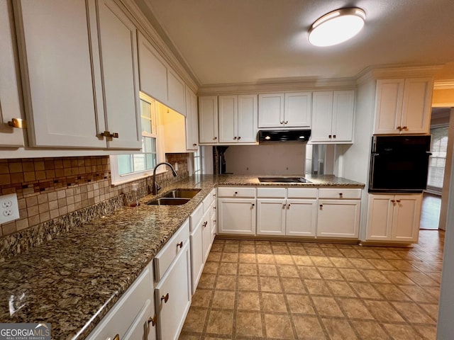kitchen featuring tasteful backsplash, under cabinet range hood, a sink, white cabinets, and black appliances