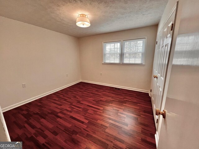 spare room with dark wood-style floors, baseboards, visible vents, and a textured ceiling