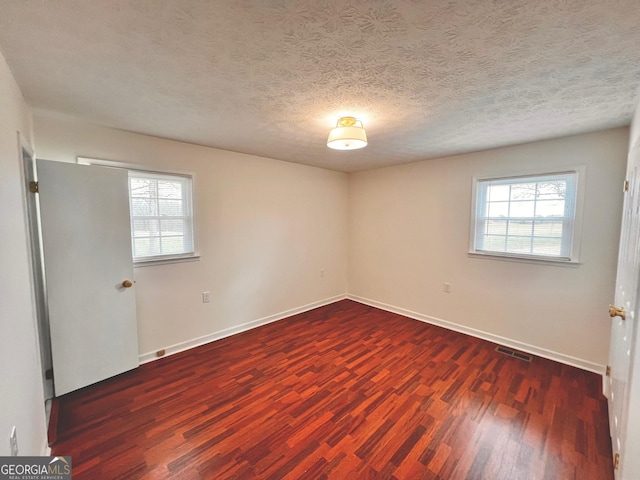 spare room featuring a healthy amount of sunlight, visible vents, baseboards, and wood finished floors