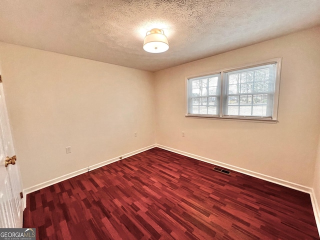 spare room featuring dark wood finished floors, a textured ceiling, baseboards, and visible vents