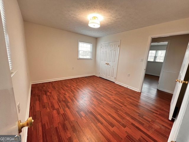 unfurnished bedroom featuring baseboards, a textured ceiling, dark wood-style floors, and multiple windows