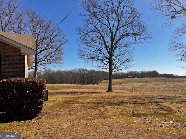 view of yard with a wooded view, a rural view, an outdoor structure, and a storage shed