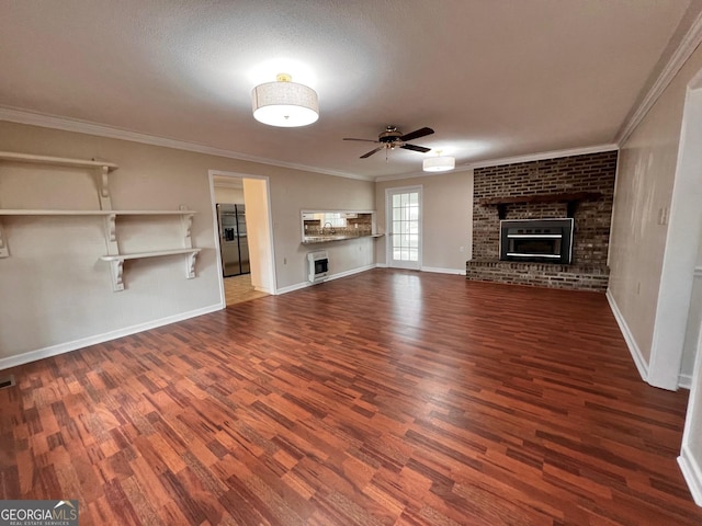 unfurnished living room with wood finished floors, ceiling fan, ornamental molding, and a brick fireplace