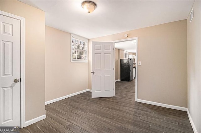 empty room featuring dark wood-style floors, visible vents, and baseboards