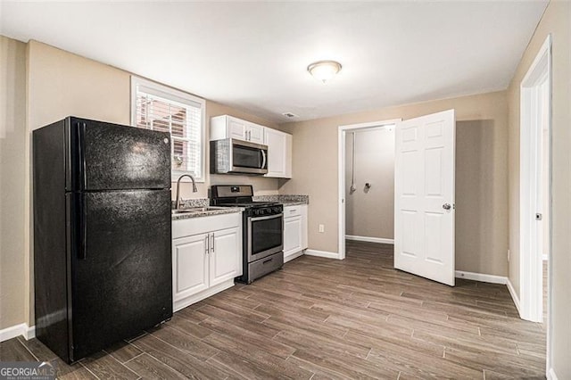 kitchen with dark wood-style flooring, stainless steel appliances, white cabinets, a sink, and baseboards