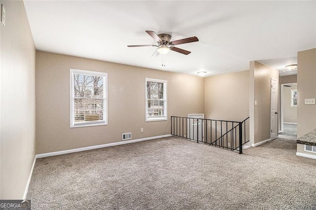 carpeted empty room featuring baseboards, visible vents, and a ceiling fan