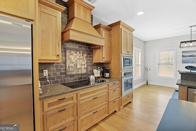 kitchen with tasteful backsplash, light wood-style flooring, dark stone countertops, custom exhaust hood, and stainless steel appliances