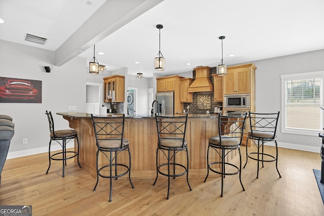 kitchen with stainless steel appliances, premium range hood, a breakfast bar area, and visible vents