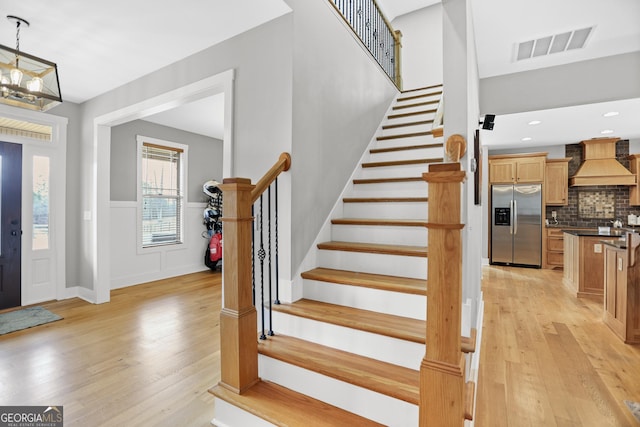 entrance foyer with stairway, a wainscoted wall, visible vents, and light wood-style flooring