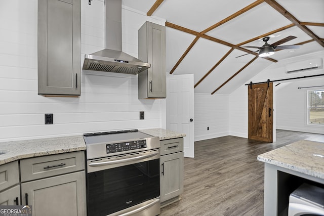 kitchen with a barn door, gray cabinetry, wall chimney range hood, a wall mounted AC, and stainless steel electric range oven