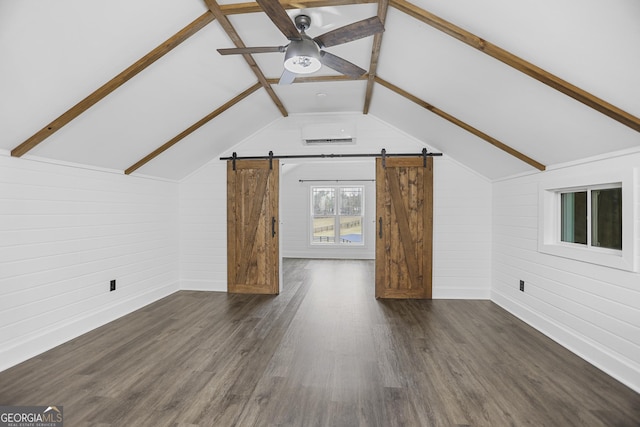 additional living space with a barn door, wooden walls, dark wood finished floors, a ceiling fan, and lofted ceiling with beams