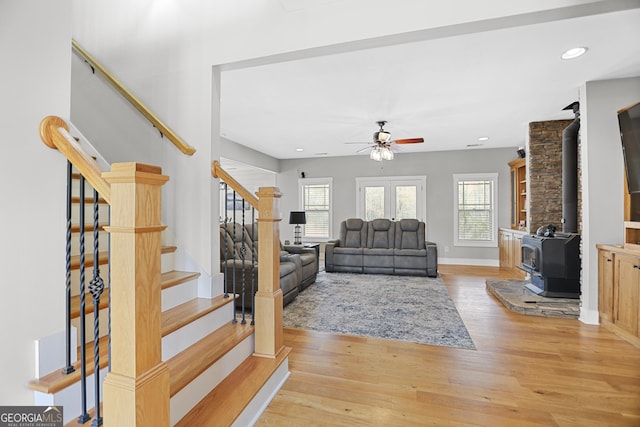 living area featuring stairs, baseboards, a wood stove, and light wood-style floors