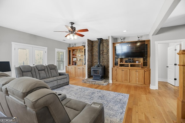 living area with a wood stove, baseboards, ceiling fan, and light wood finished floors