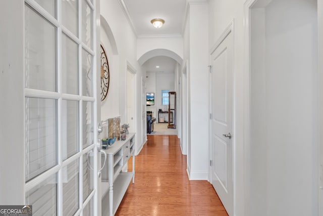 corridor featuring arched walkways, ornamental molding, and light wood-type flooring