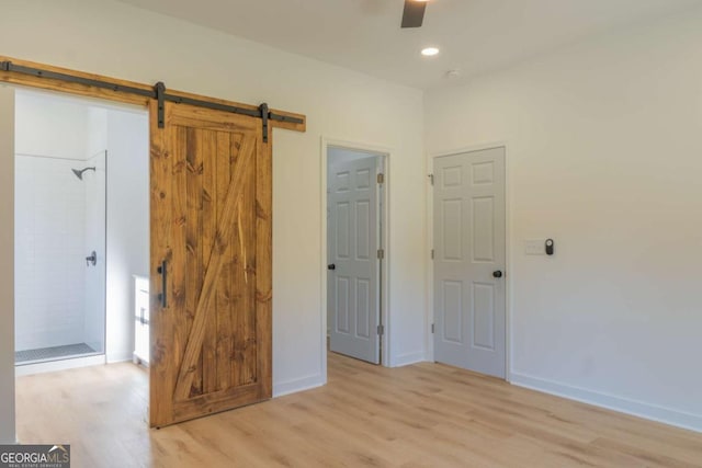 unfurnished bedroom featuring wood finished floors, baseboards, and a barn door