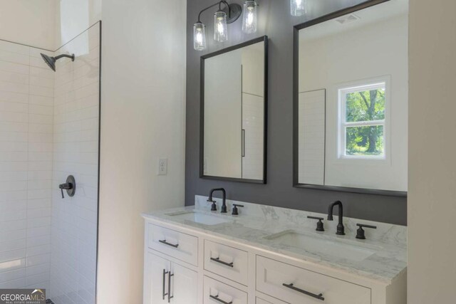 bathroom featuring visible vents, a sink, a tile shower, and double vanity