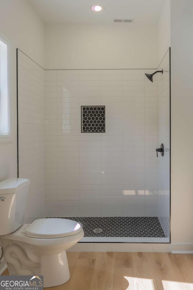 bathroom with visible vents, toilet, wood finished floors, a tile shower, and recessed lighting