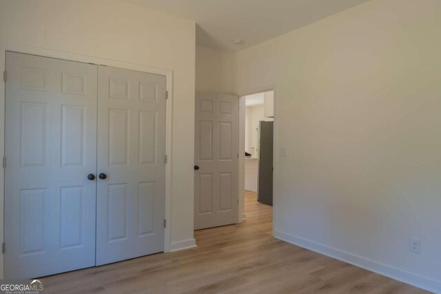 unfurnished bedroom featuring light wood-style floors, baseboards, a closet, and freestanding refrigerator