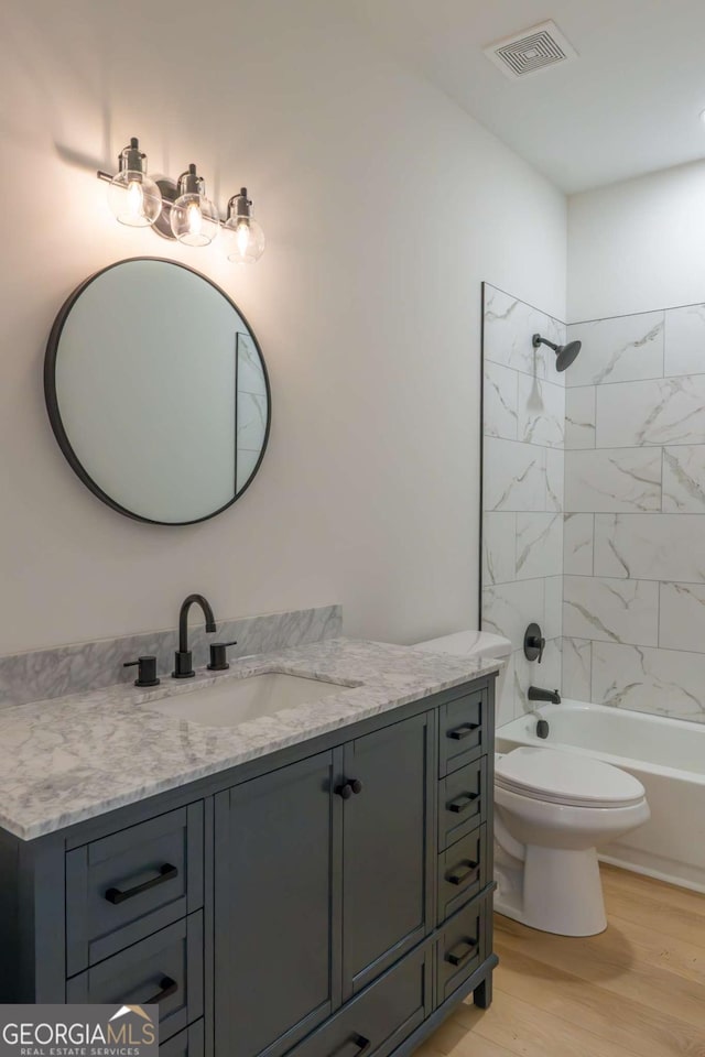 bathroom with visible vents, toilet, wood finished floors, vanity, and shower / bathing tub combination