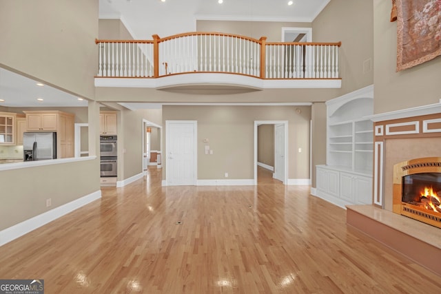 unfurnished living room with baseboards, a tiled fireplace, a high ceiling, crown molding, and light wood-style floors