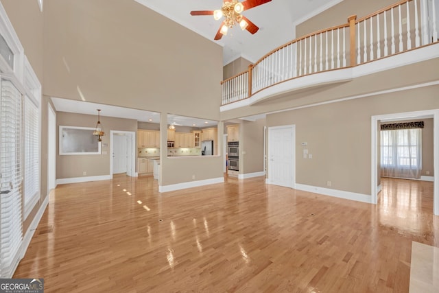 unfurnished living room with ceiling fan, light wood-type flooring, a towering ceiling, and baseboards