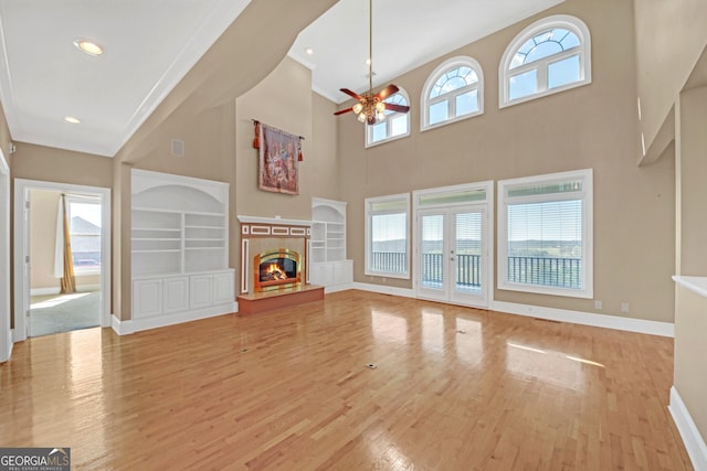 unfurnished living room featuring wood finished floors, baseboards, built in features, french doors, and a glass covered fireplace