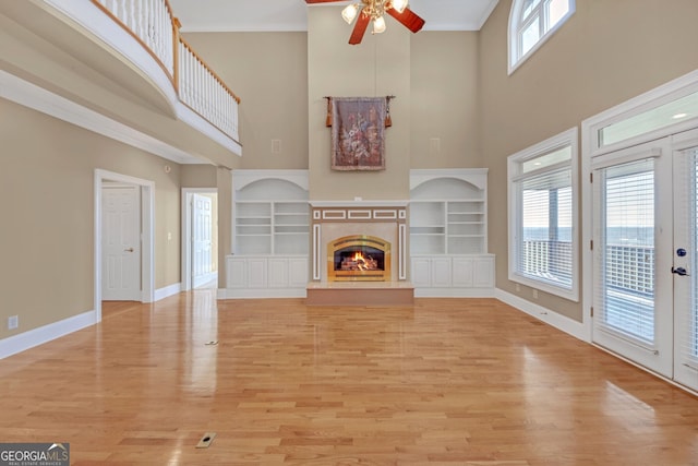 unfurnished living room featuring built in features, light wood-style floors, a glass covered fireplace, ornamental molding, and baseboards