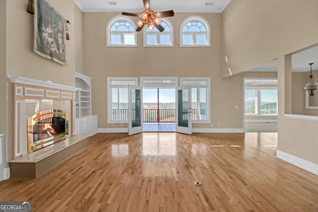 unfurnished living room with wood finished floors, a ceiling fan, a high end fireplace, baseboards, and crown molding