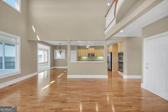 unfurnished living room featuring a high ceiling, light wood-type flooring, visible vents, and baseboards