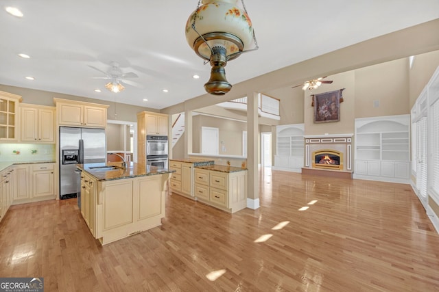 kitchen with ceiling fan, dark stone countertops, cream cabinets, stainless steel appliances, and a sink