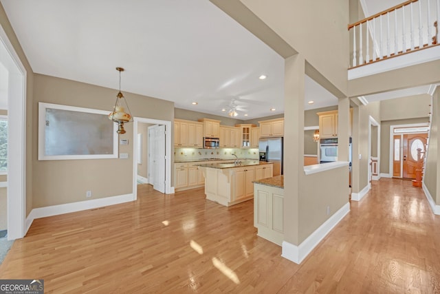 kitchen with stainless steel appliances, light wood-style flooring, cream cabinets, a kitchen island with sink, and baseboards