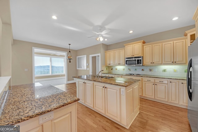 kitchen featuring light stone counters, cream cabinets, appliances with stainless steel finishes, a ceiling fan, and a sink