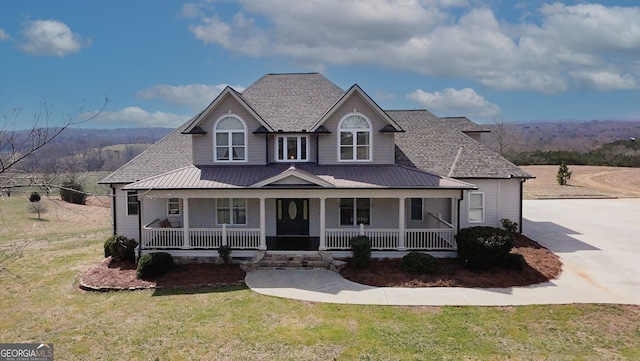 view of front facade with roof with shingles, covered porch, a standing seam roof, metal roof, and a front lawn