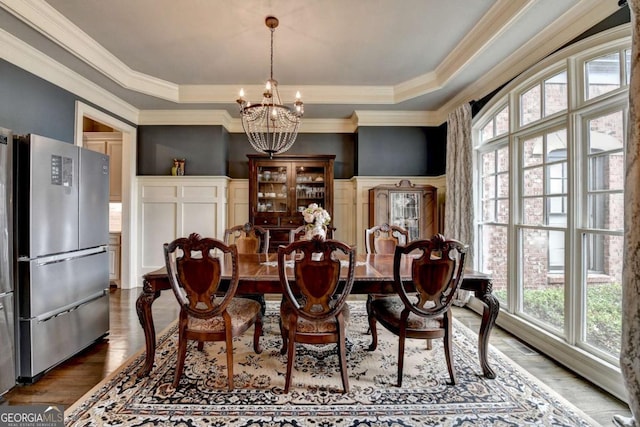 dining room featuring a chandelier, wood finished floors, wainscoting, a tray ceiling, and crown molding