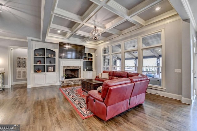 living room with coffered ceiling, wood finished floors, beam ceiling, a stone fireplace, and a notable chandelier